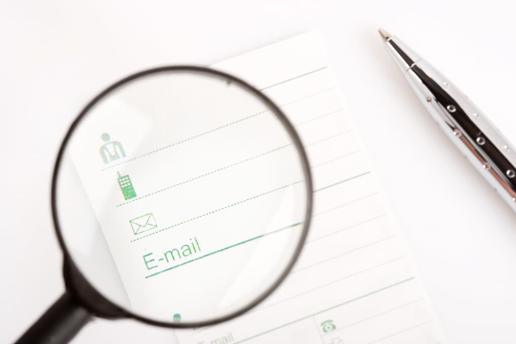 Image of a magnifying glass against a background of face, phone, and email icons on a piece of paper.